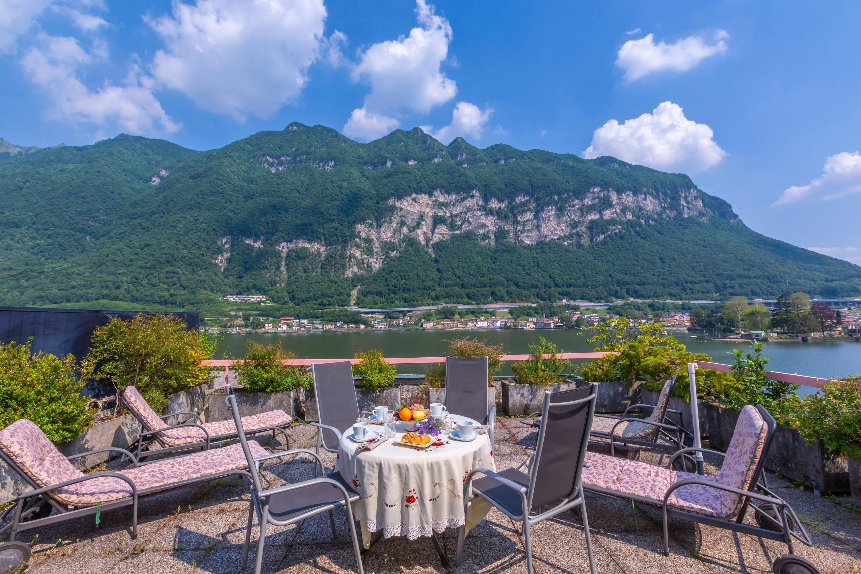 A terrace with a table set for two, overlooking a river and mountains.