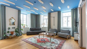Ein geräumiges Wohnzimmer mit blauer Decke, einem gemusterten Teppich, einer Couch, einem Sessel und einem Couchtisch.