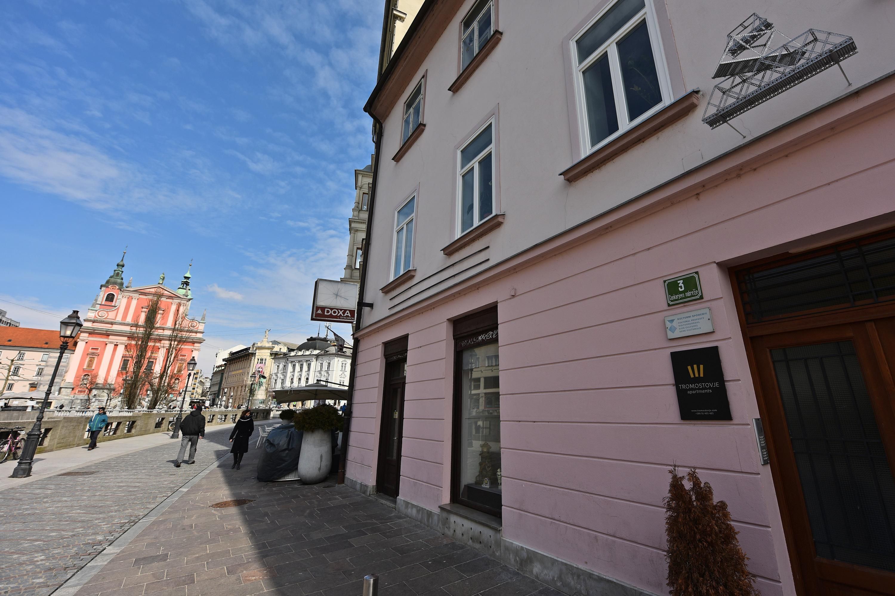 A pink building with a sign indicating it's a hotel. There are people walking on the sidewalk, and a large potted plant is visible.