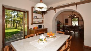 Un coin repas avec une table en marbre, des chaises en bois, un panier de fruits et, au fond, une cuisine.