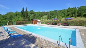 Une piscine entourée de verdure et d’un petit bâtiment, avec des chaises longues et des parasols à proximité.