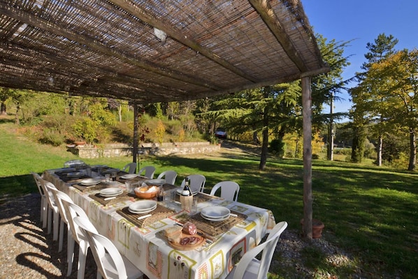 Enjoy a meal under the shade of a pergola, surrounded by lush greenery and a stone wall.