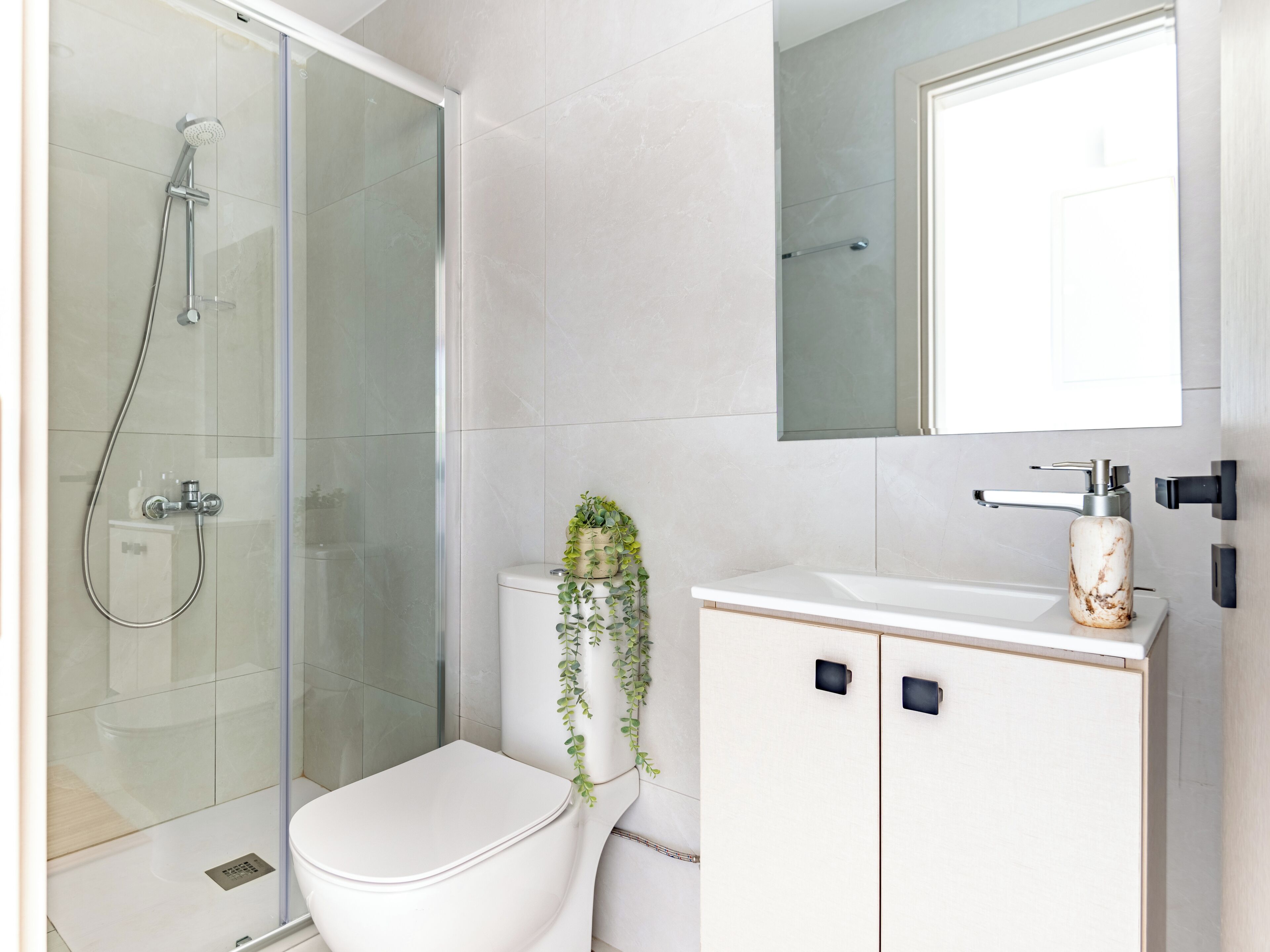 Un bagno moderno con cabina doccia in vetro, un water, un lavandino con dispenser di sapone dall’aspetto marmorizzato e uno specchio sopra il lavandino.