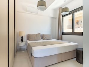 Une chambre à coucher moderne avec un grand lit, une table de chevet avec une lampe et une fenêtre avec des rideaux.