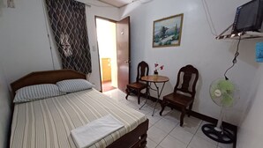 A bedroom with a bed, a small table with chairs, a wall-mounted TV, and a standing fan. - OYO 909 Jc Affordable Transient (Tagaytay)