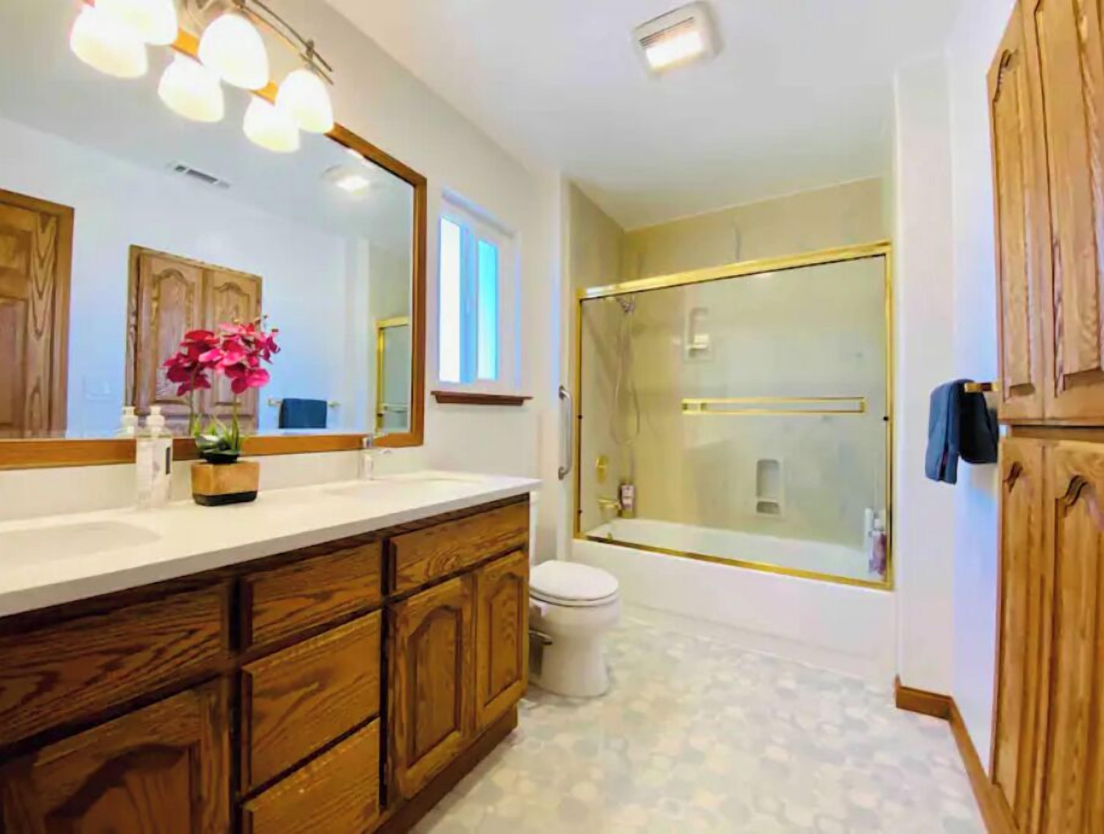 Une salle de bain avec un meuble-lavabo en bois, un grand miroir, une cabine de douche en verre et des toilettes.