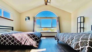 Une chambre avec deux lits, une grande fenêtre en arc de cercle et une vue sur l’extérieur.