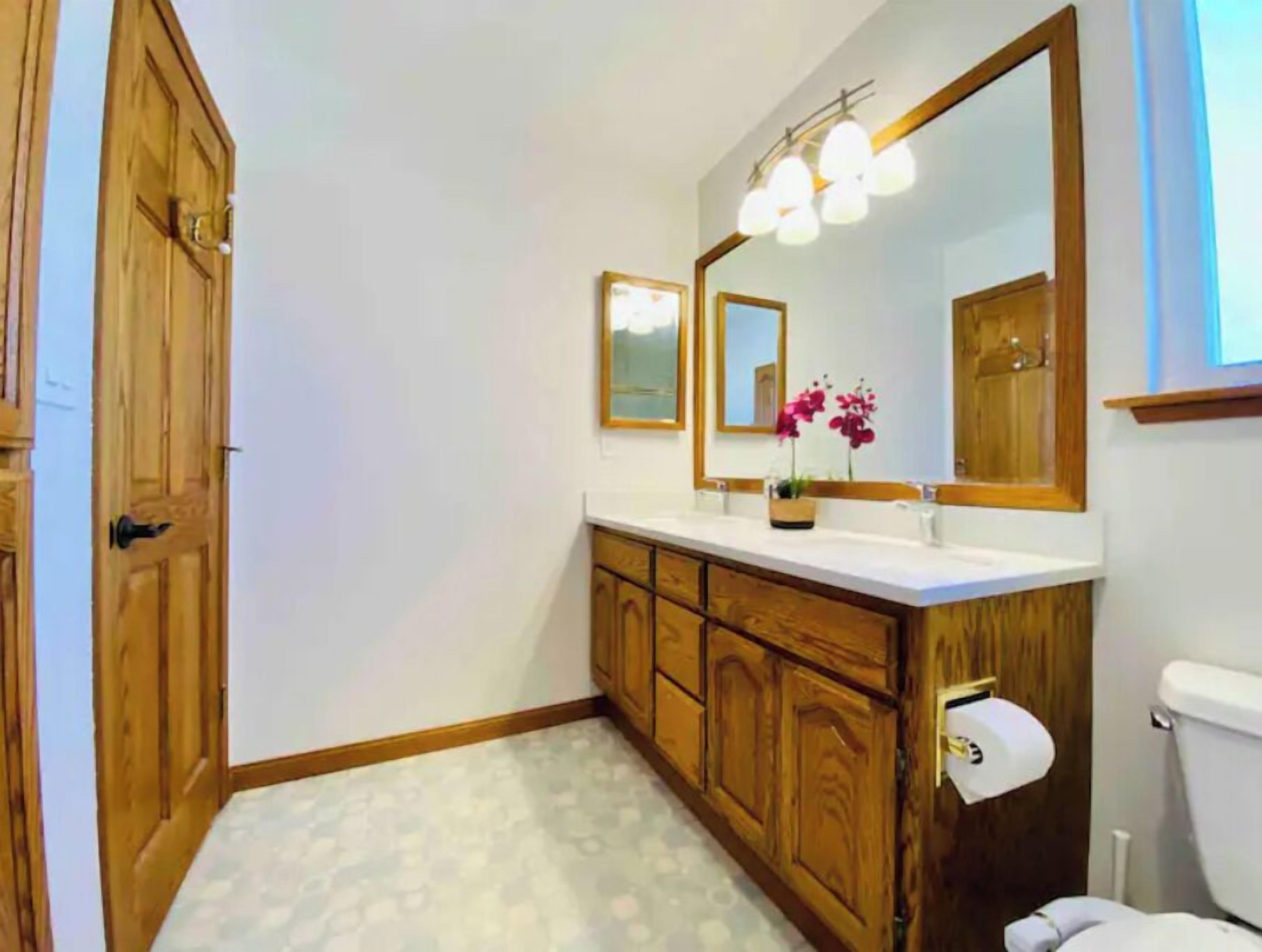 Ein Badezimmer mit Holzsärchen, einem weißen Waschbecken, einem großen Spiegel und einer Toilette.