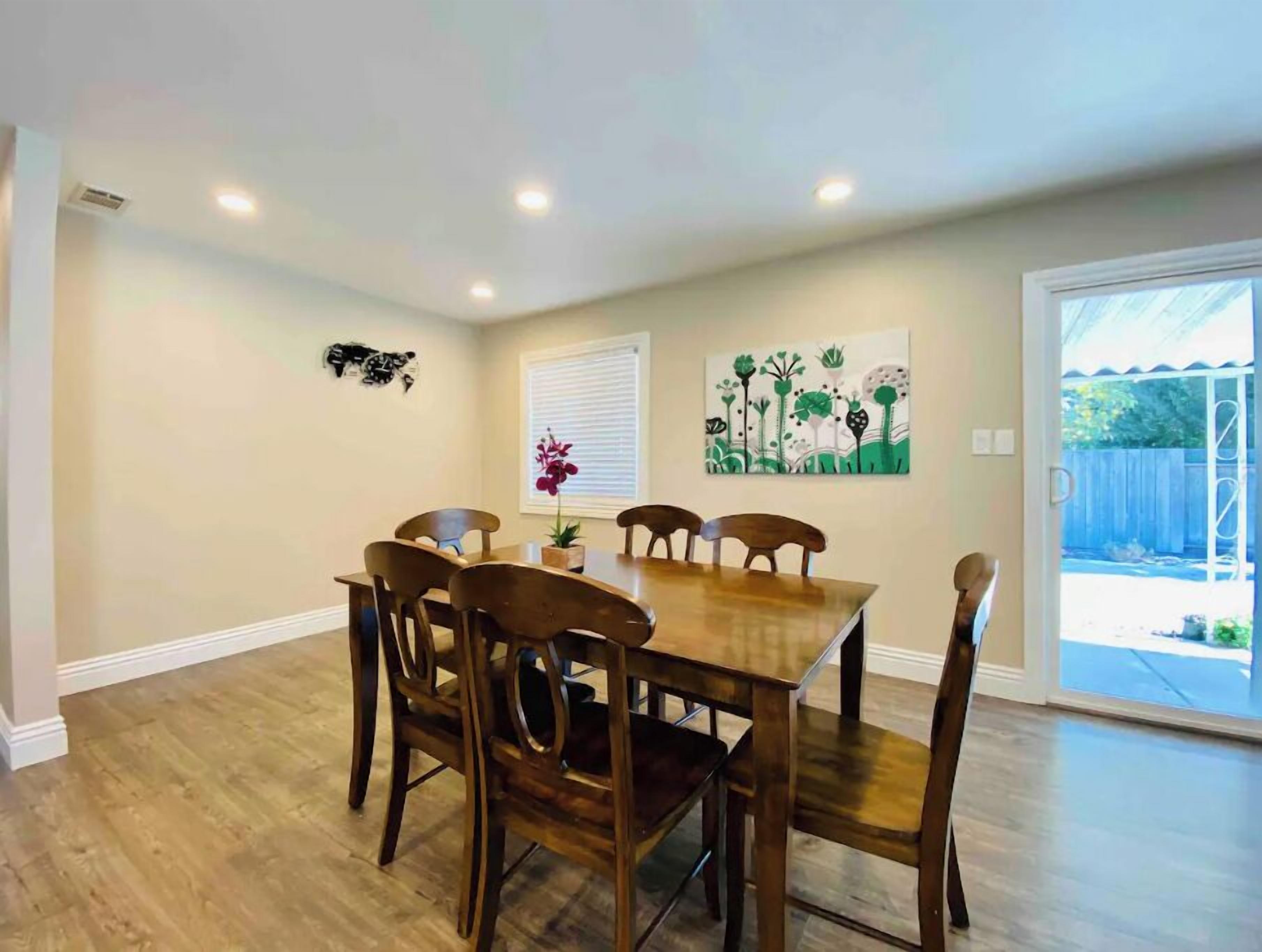 A dining area with a wooden table and chairs, a window with blinds, and a door leading to an outdoor area.