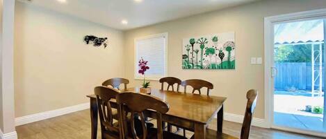 A dining area with a wooden table and chairs, a window with blinds, and a door leading to an outdoor area.