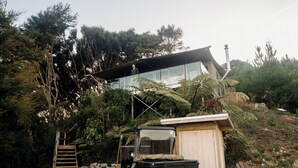 Ein modernes Haus mit Glasanbau, einem Fahrzeug und einer Holzterrasse.