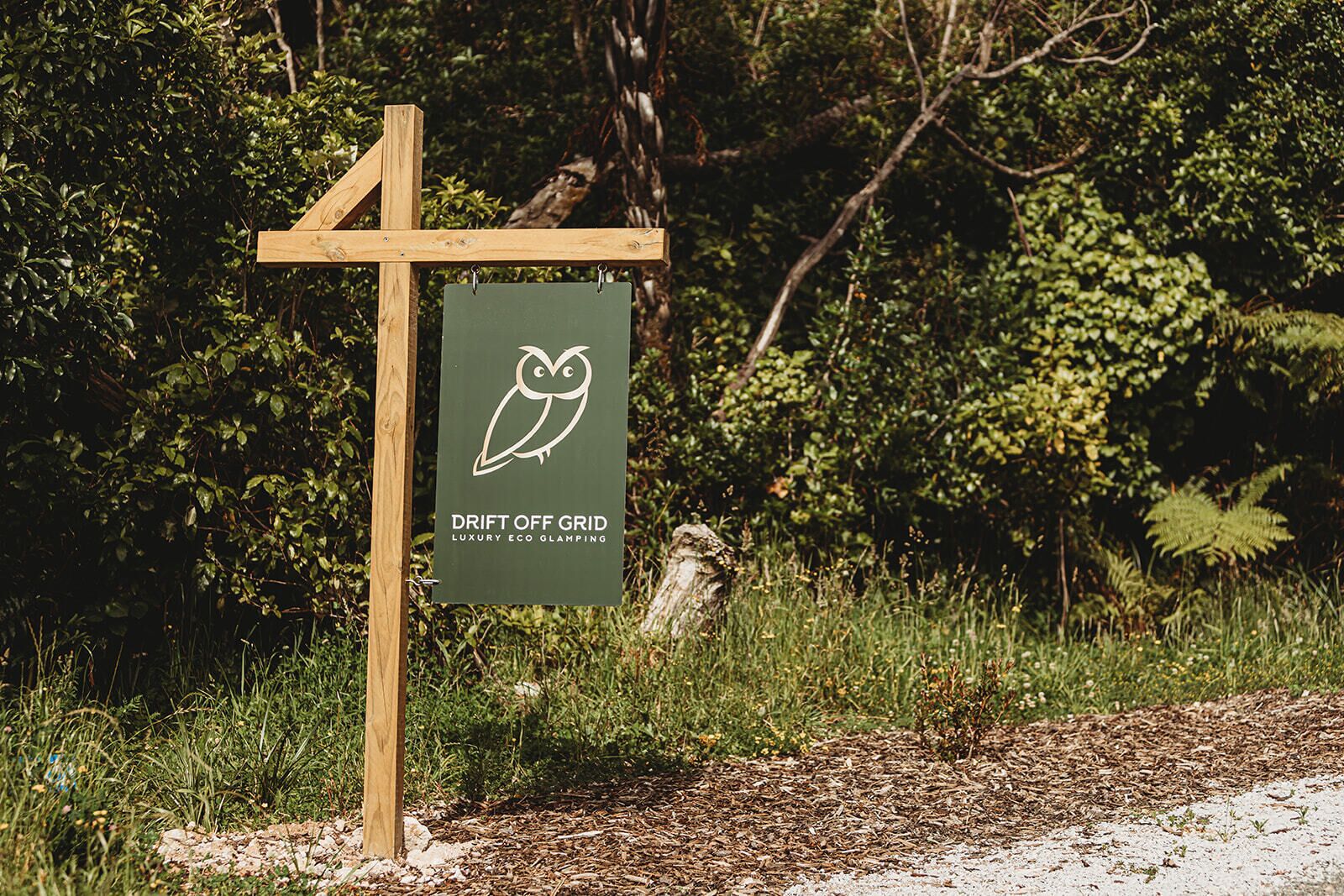 Une enseigne pour « Drift Off Grid Luxury Eco Glamping », avec un poteau en bois et un panneau vert.