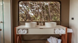 Une salle de bain avec deux lavabos, une fenêtre donnant sur les arbres et des serviettes posées sur le comptoir.