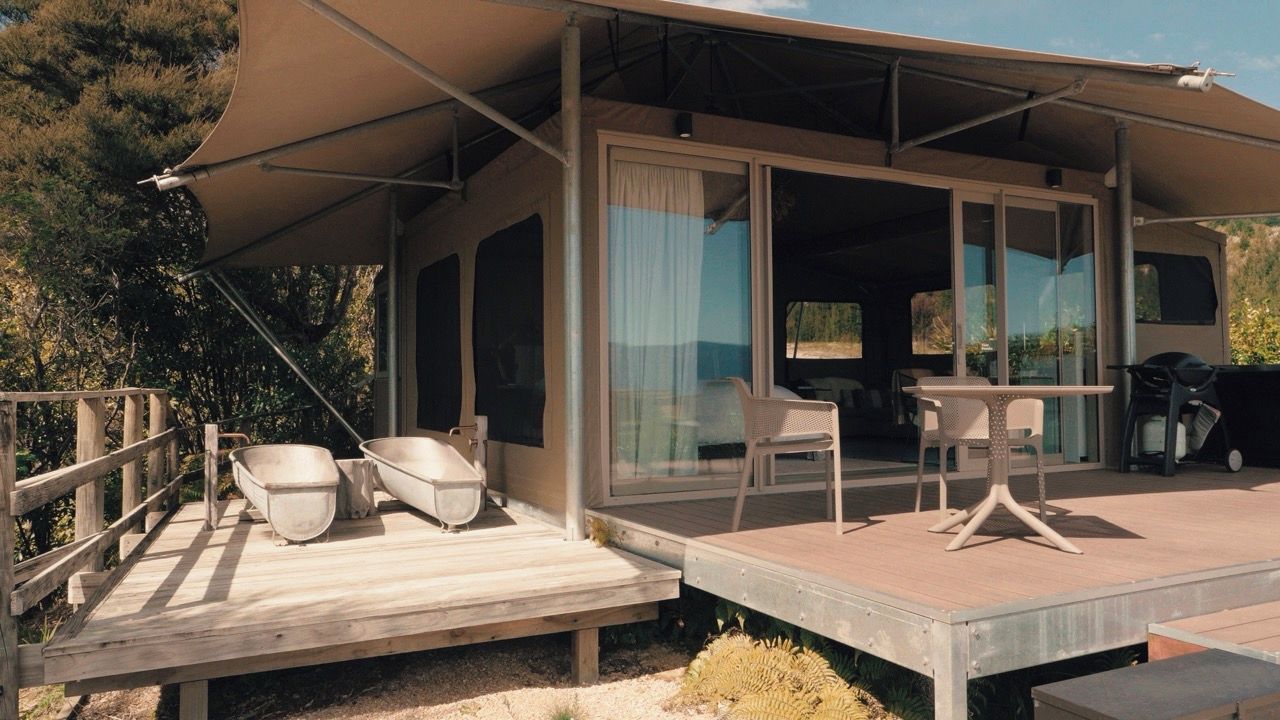 A covered outdoor area with a table and chairs, a wooden deck, and a glass door leading inside.