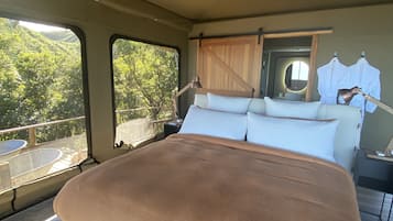 Ein geräumiges Schlafzimmer mit einem großen Bett, einem Nachttisch, einem Spiegel und Blick auf Grünfläche.