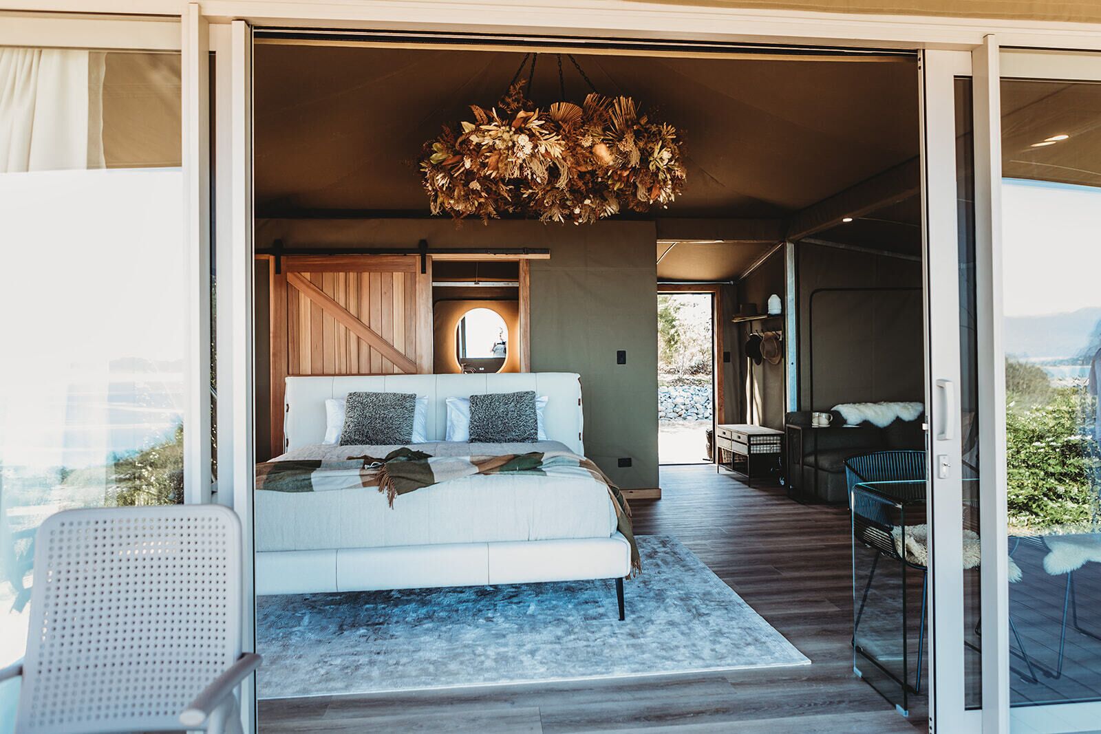 A bedroom with a large bed, a hanging light fixture, and a view of the outdoors.