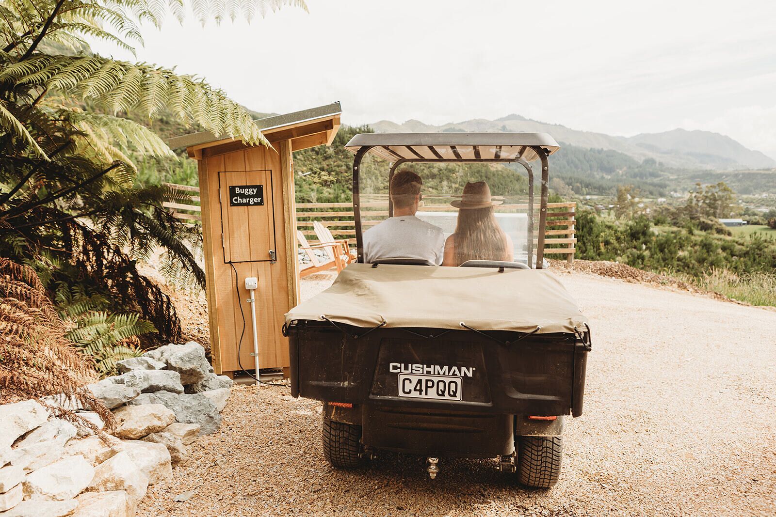 A vehicle parked at a campsite with a wooden cabin labeled "Buggy Charger" and a sign reading "CUSHMAN CAPOO".
