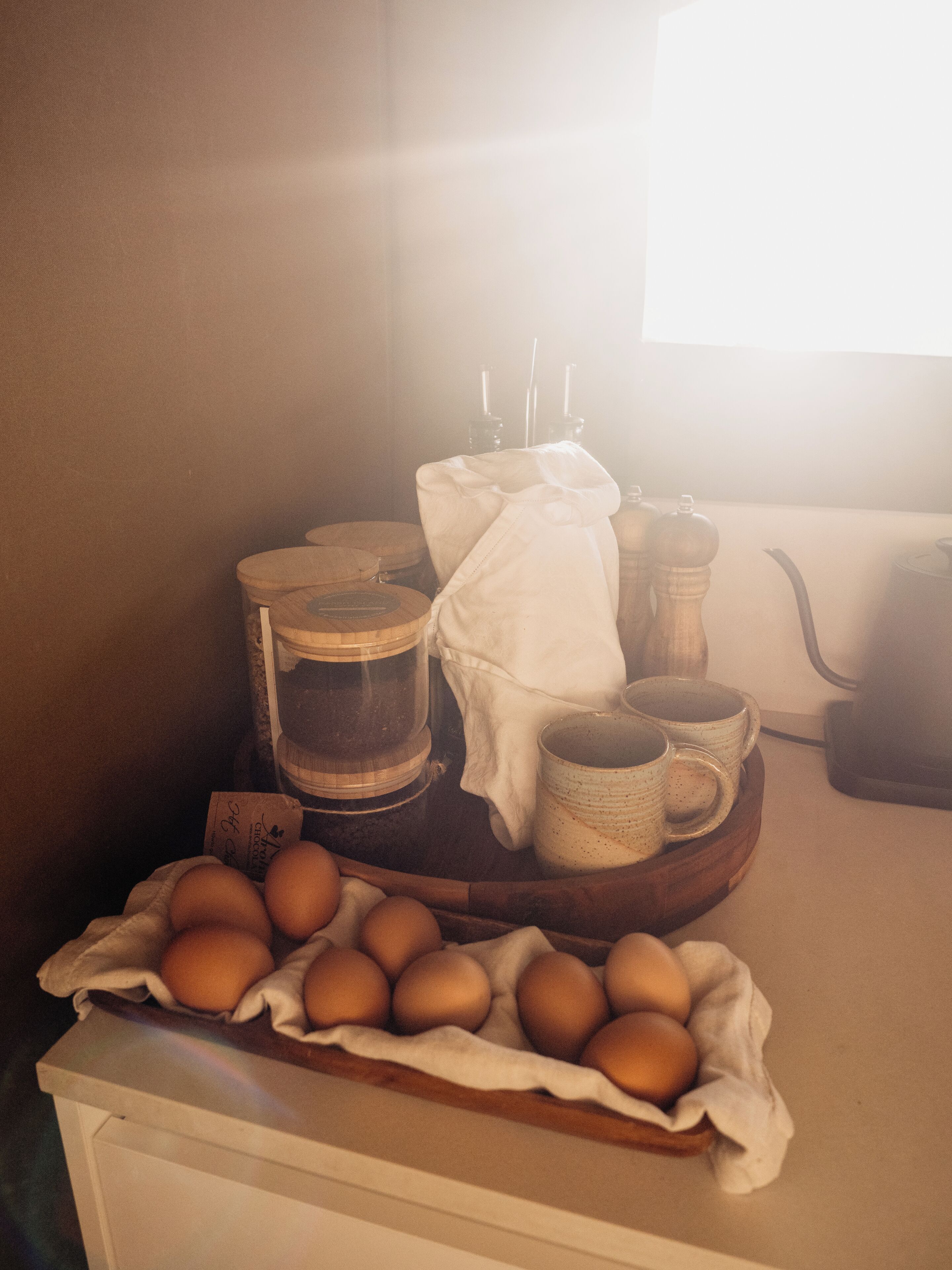 Een keukentafel met een houten dienblad waarop eieren, een koffiezetapparaat en een theepot staan.