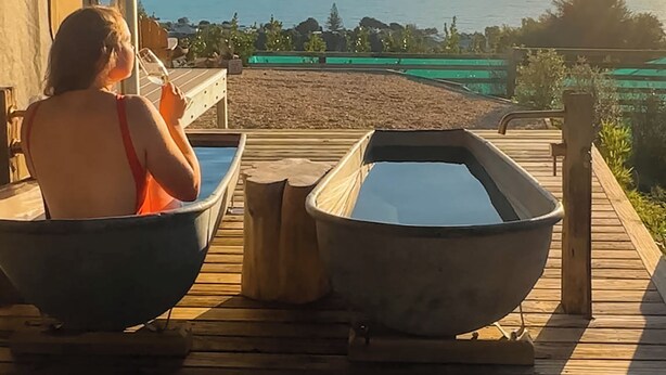 Une terrasse en bois avec deux bains à remous et une personne se relaxant.