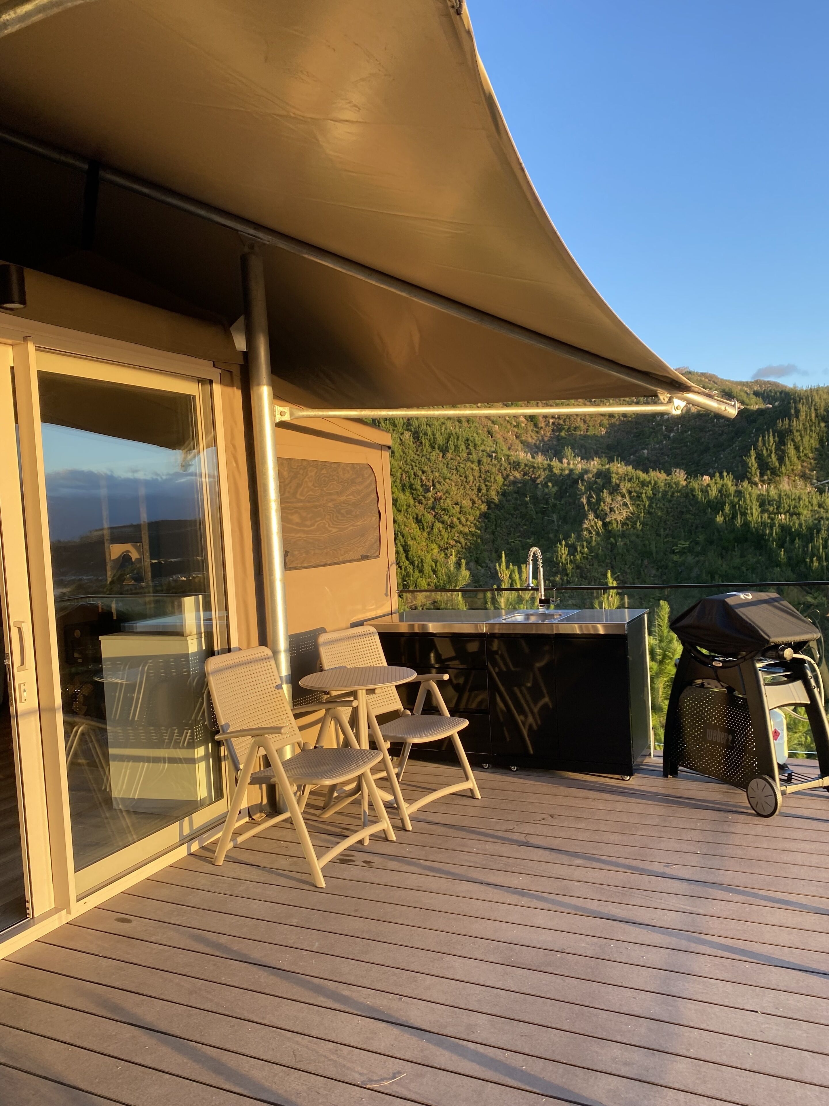 An outdoor deck with a table and chairs, a grill, and a view of a forested hillside.
