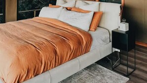 Une chambre moderne avec un grand lit, une tête de lit en bois et une vue sur les arbres par la fenêtre.