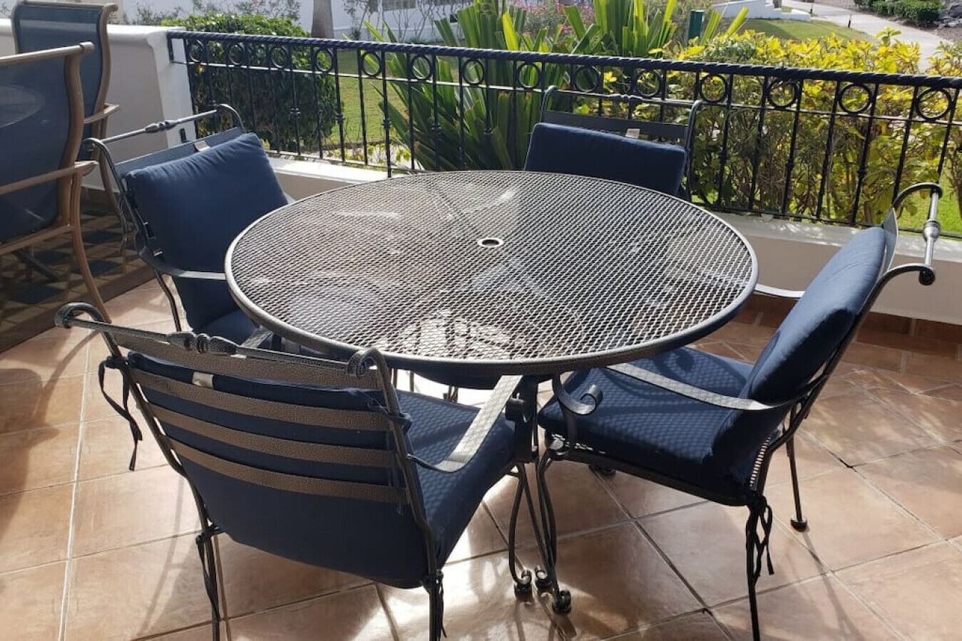 Un tavolo rotondo in metallo con quattro sedie, un pavimento piastrellato e una ringhiera in metallo nero.