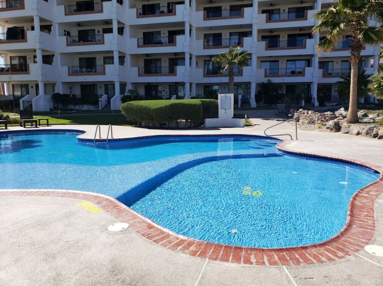 A swimming pool with a brick border, surrounded by a building with multiple balconies.