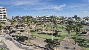 Ein Golfplatz mit Palmen, einem Weg und Gebäuden im Hintergrund.
