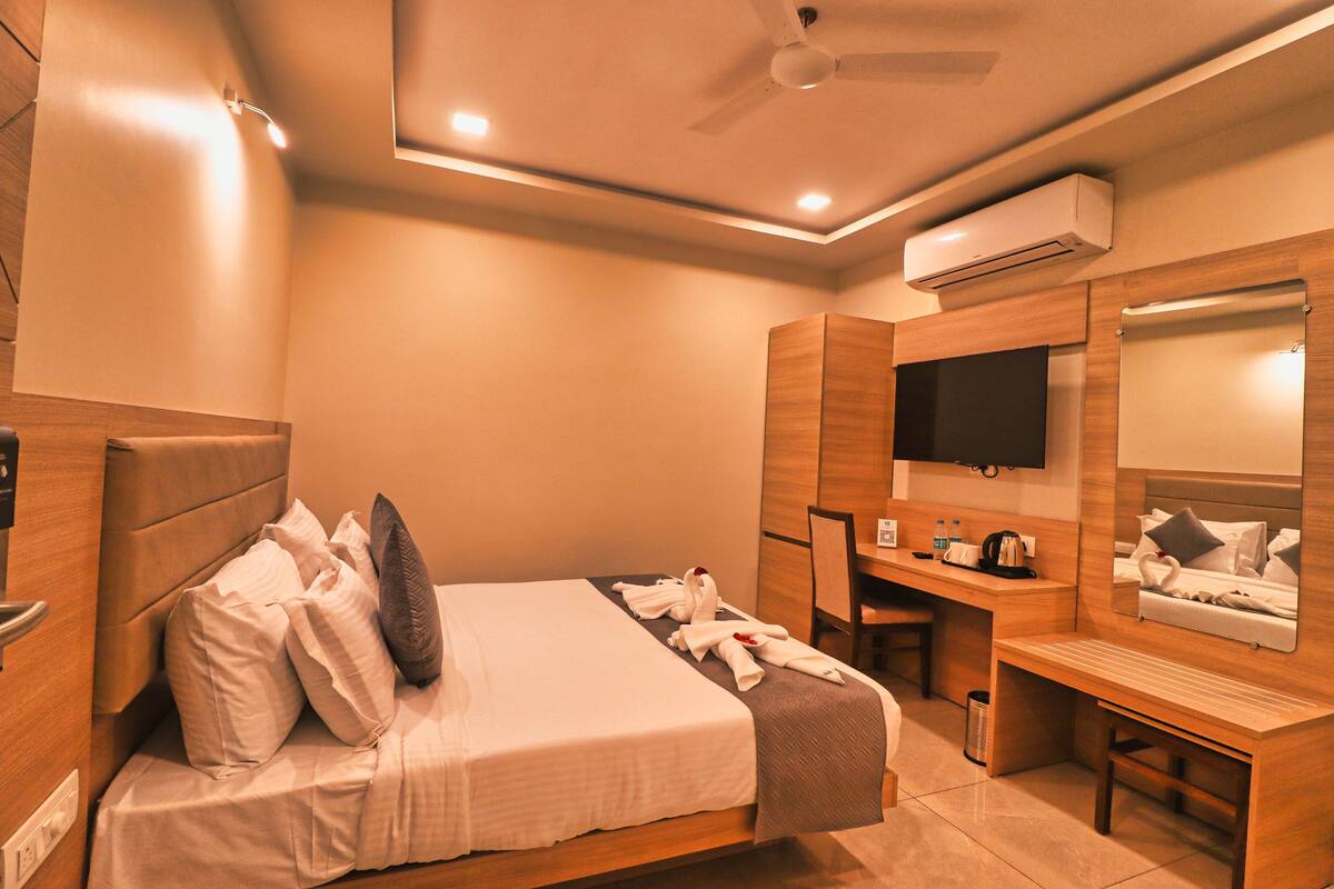 A hotel room with a bed, desk, chair, TV, and air conditioning unit.