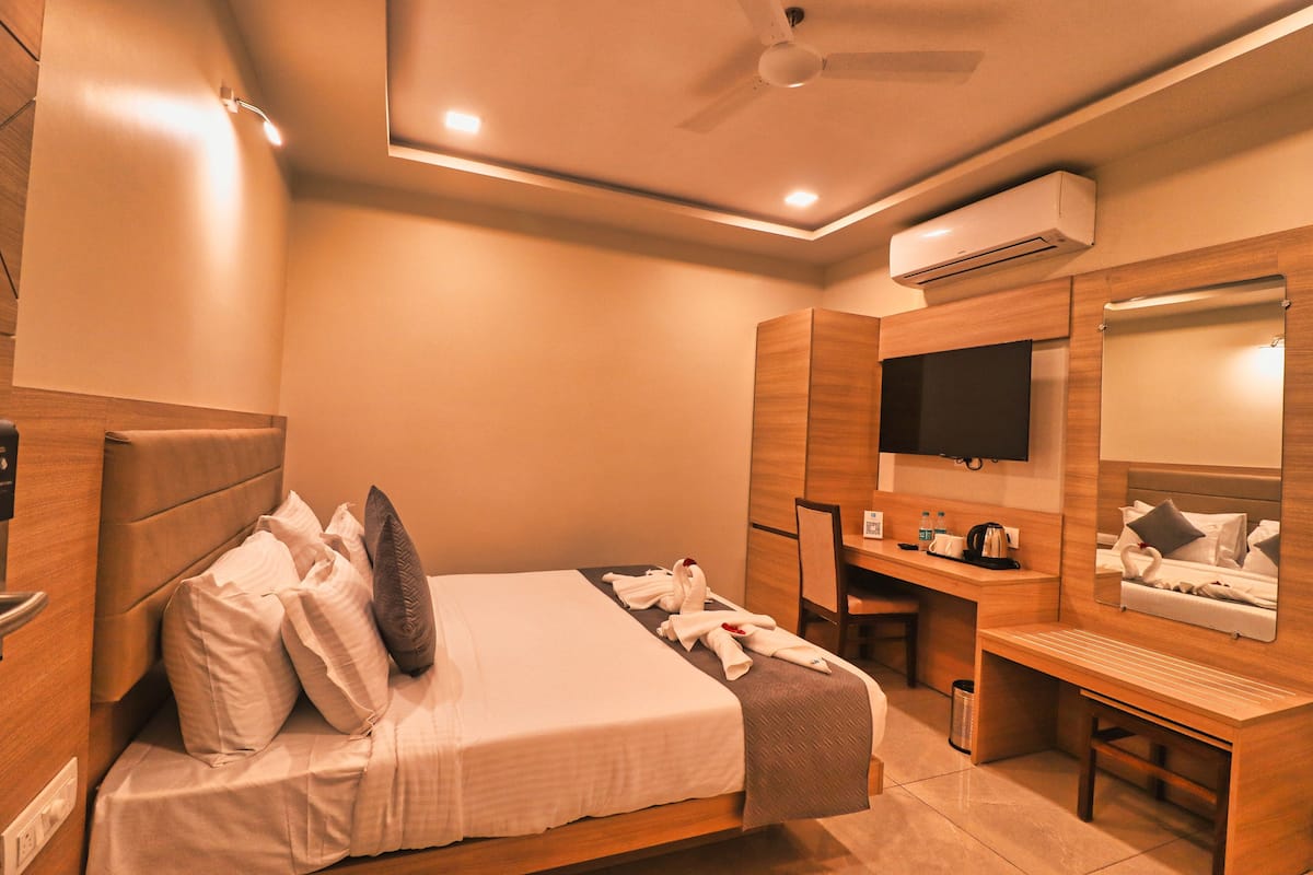 A hotel room with a bed, desk, chair, TV, and air conditioning unit.