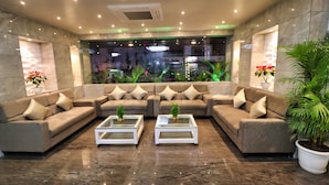 Um lobby moderno com um sofá em seção, duas mesas de centro de vidro e plantas em vasos.