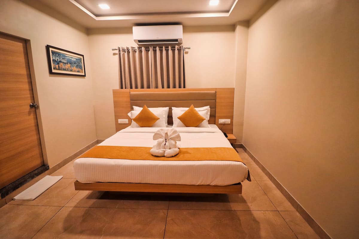 A hotel room with a bed, a picture on the wall, an air conditioning unit, and a curtain.