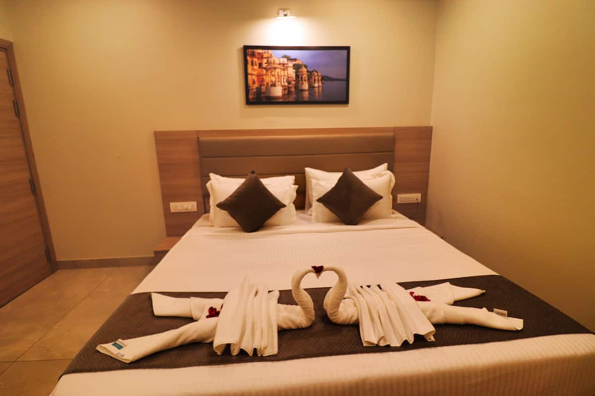 A hotel room with a neatly made bed, pillows, and a decorative swan towel arrangement.