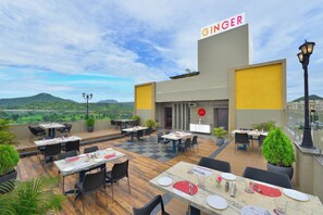 An outdoor restaurant with tables and chairs, a view of the landscape, and a building with a sign reading 'GINGER'. - Ginger Udaipur Hiran Magri (Udaipur)