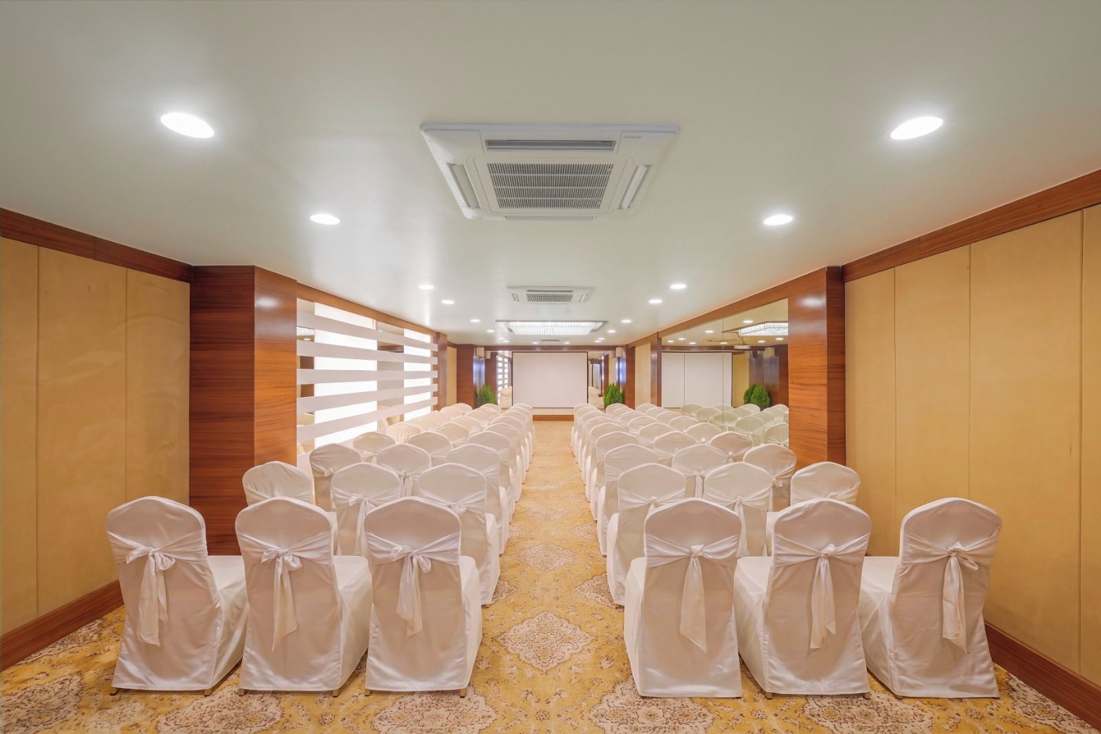 Ein Hotelkonferenzraum mit Reihen von Stühlen, einer Projektionsleinwand und einem Teppichboden.