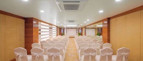 A hotel conference room with rows of chairs, a projector screen, and a carpeted floor.