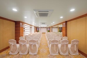 A hotel conference room with rows of chairs, a projector screen, and a carpeted floor. - Ginger Udaipur Hiran Magri (Udaipur)