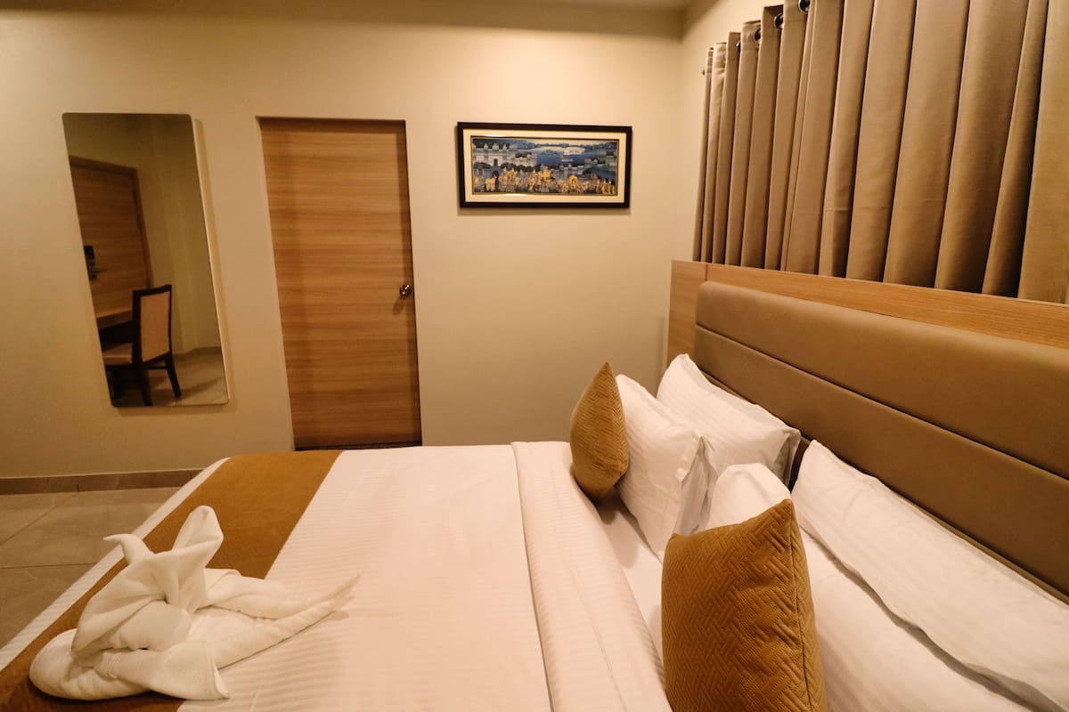 A hotel room with a bed, a framed picture on the wall, a door, and a mirror.