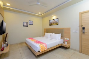 A hotel room with a bed, a bedside table, a television, and a door. - Ginger Udaipur Hiran Magri (Udaipur)