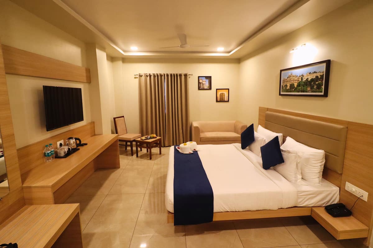 A hotel room with a bed, bedside tables, a desk, a chair, a TV, and a painting on the wall.