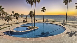 A swimming pool with a curved design, surrounded by palm trees and a view of the ocean at sunset.