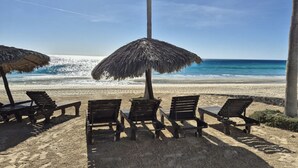 A beach with wooden lounge chairs and a thatched umbrella, overlooking the ocean.