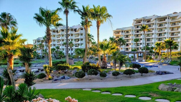 A hotel with multiple floors, palm trees, and a well-maintained garden with flowers and shrubs.