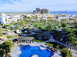 Un complexe hôtelier doté d’une grande piscine, de palmiers et offrant une vue sur la mer.