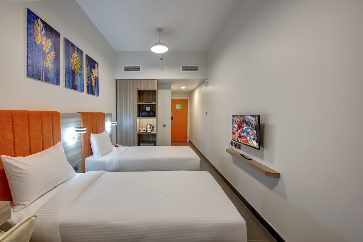 A hotel room with two beds, a television, artwork on the wall, and a hallway leading to a bathroom.