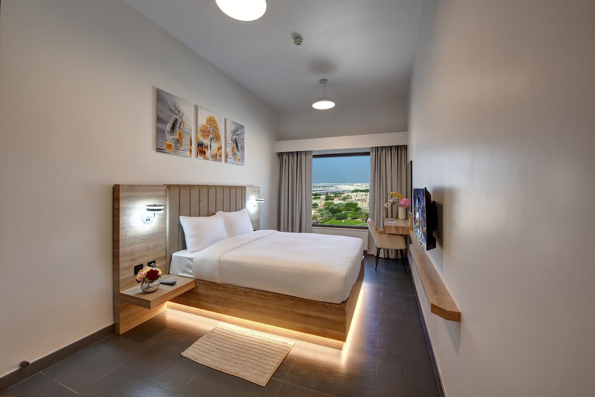 A modern hotel room with a large bed, bedside tables, artwork on the walls, and a view of the cityscape through the window.
