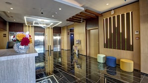 Eine moderne Lobby mit einem Marmor-Rezeptionsschalter, Aufzügen und einer dekorativen Vase mit Blumen.