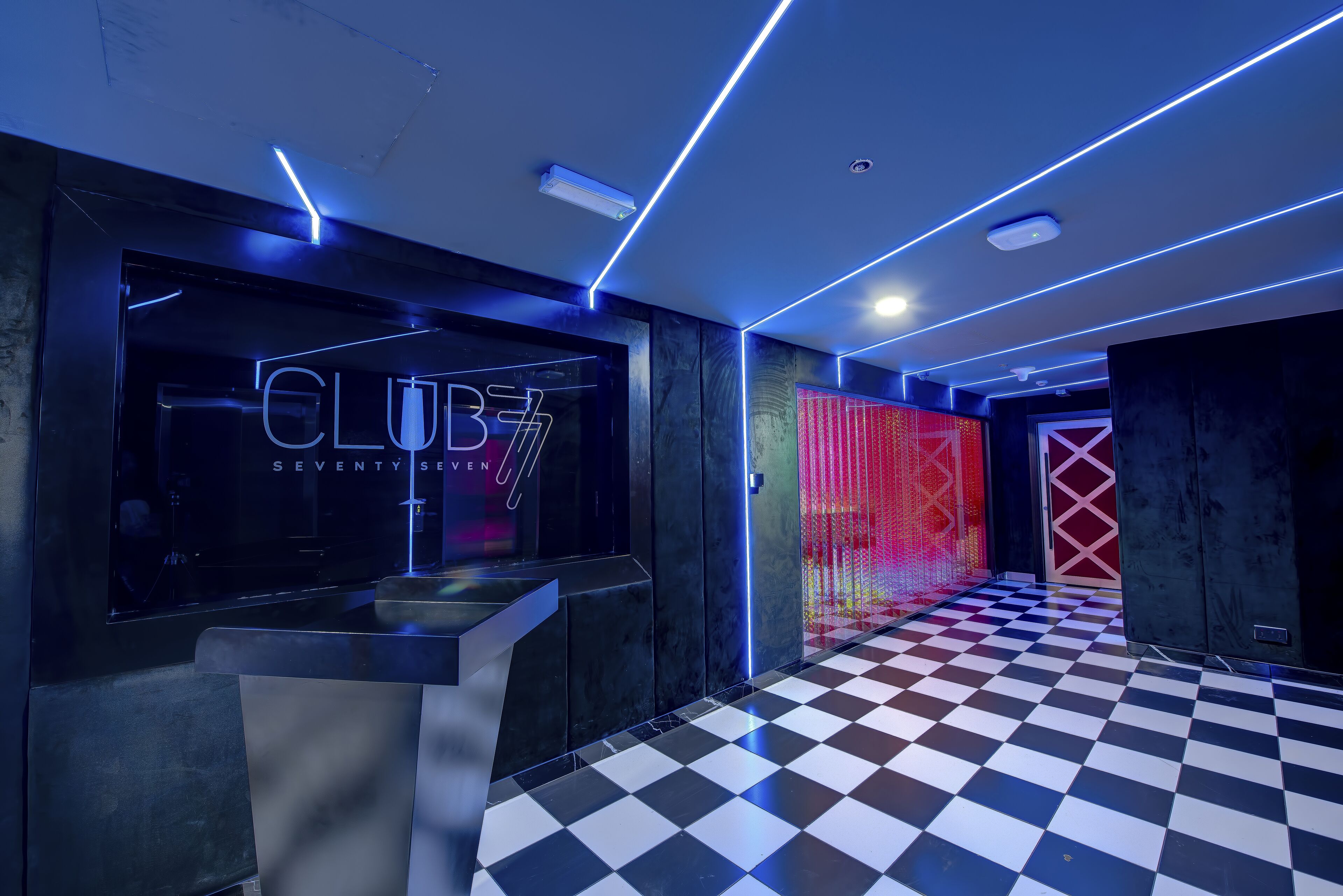 Un vestíbulo moderno con piso a cuadros, una mesa de recepción y un letrero de neón que dice "CLUB 7".