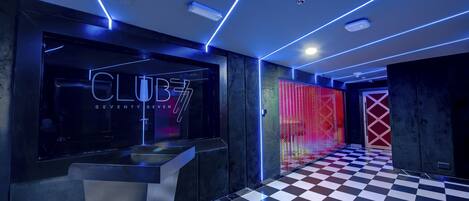 Un vestíbulo moderno con piso a cuadros, una mesa de recepción y un letrero de neón que dice "CLUB 7".