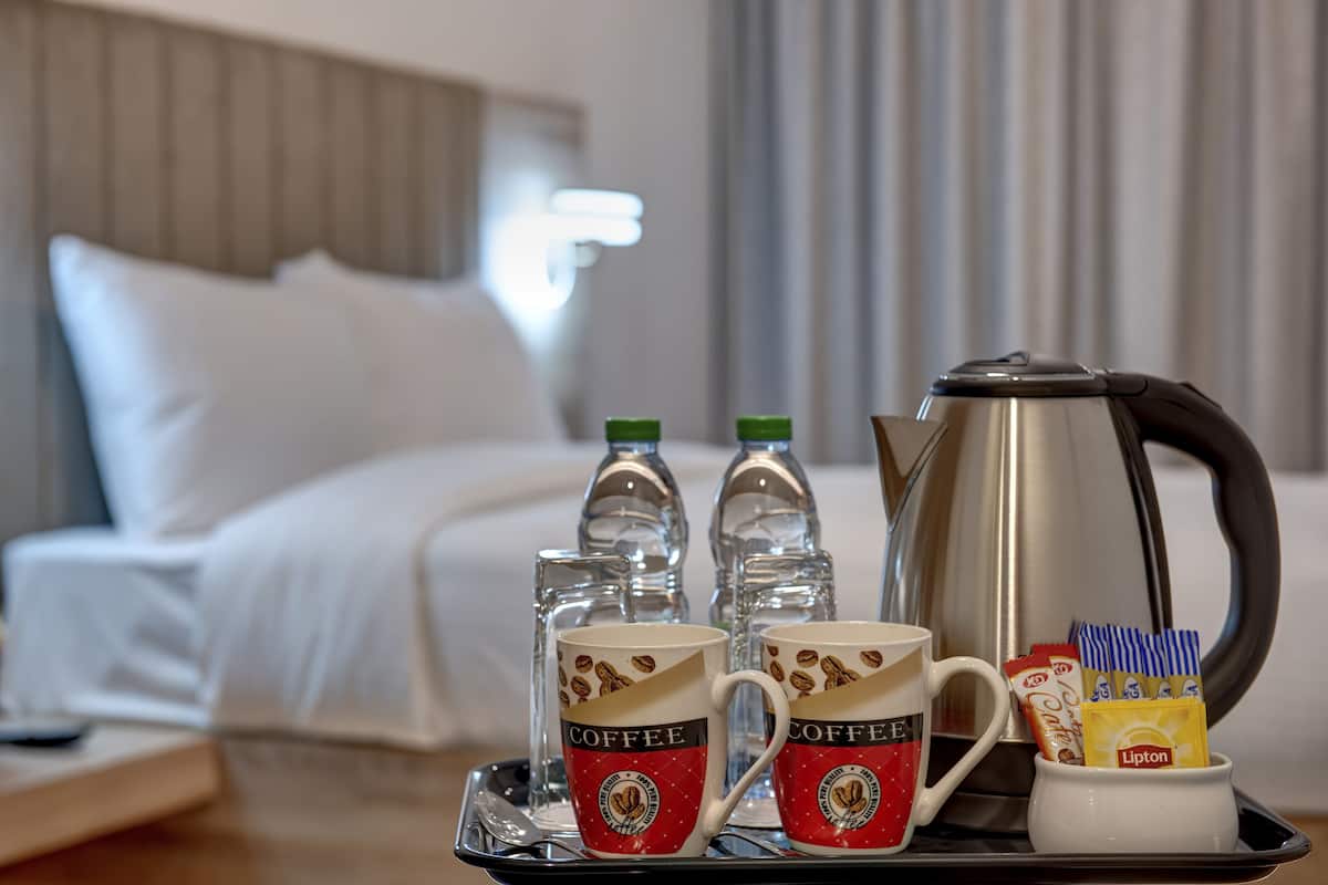 A tray with two coffee mugs, two glass bottles, a kettle, and some Lipton tea packets on a hotel room table.